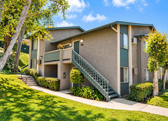 A beige house with green shutters and a staircase leading to the second floor.