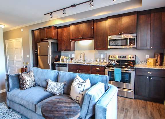 a living room with a blue couch in front of a kitchen  at Victoria Park and V2 Apartments, St. Paul, MN