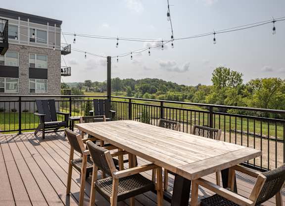 A wooden table with chairs is set up on a deck with a view of a green landscape.