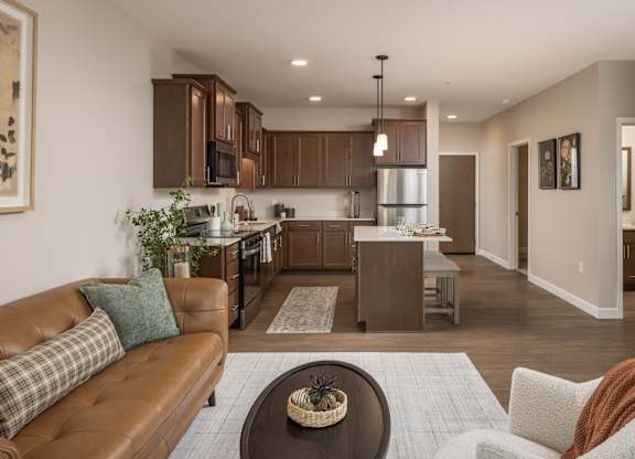 A brown leather couch with a green pillow is in the foreground of a modern kitchen and living room.