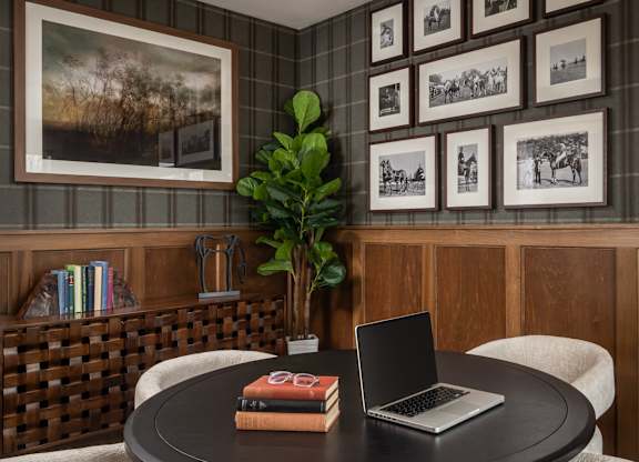 A round table with a laptop and a book on it with a potted plant behind it.