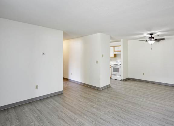 A spacious room with a ceiling fan and a kitchenette in the background.