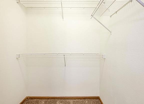 A white wall with a metal rack on top and a brown carpet on the floor.