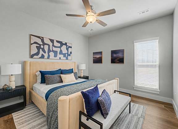 A bedroom with a bed, a ceiling fan, and a painting on the wall.