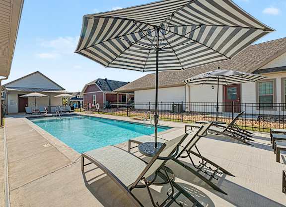 A striped umbrella is over a lounge chair by a pool.