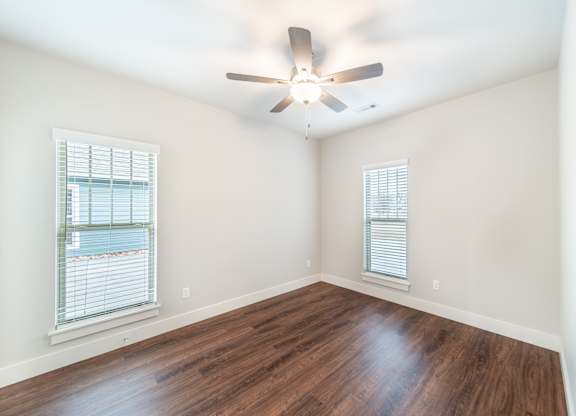 A room with a ceiling fan and two windows.