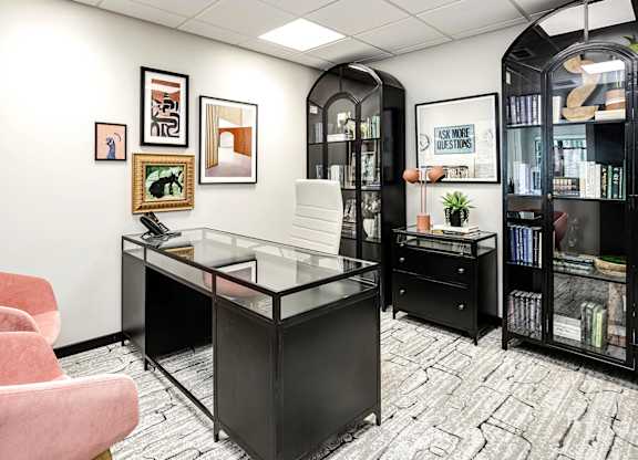 A black and white office with a glass desk and a pink chair.