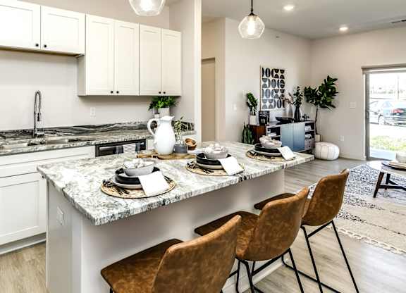 A kitchen with a marble countertop and brown chairs.