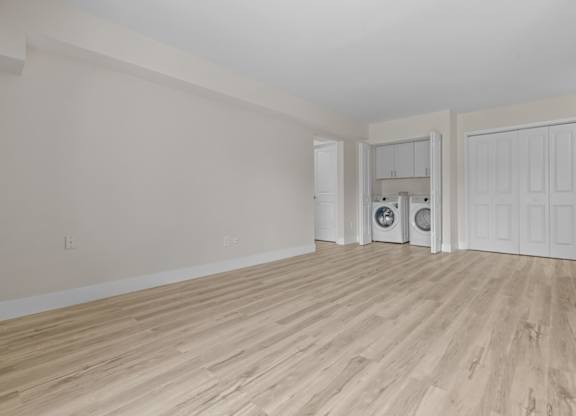 the living room and laundry room of an apartment with white walls and wood flooring at Sunnymede Apartments - Troy, MI, Michigan, 48084