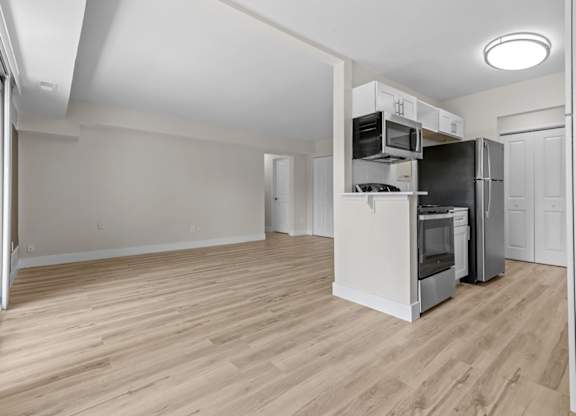 an empty living room with a kitchen with a refrigerator and a microwave at Sunnymede Apartments - Troy, MI, Troy, MI, 48084