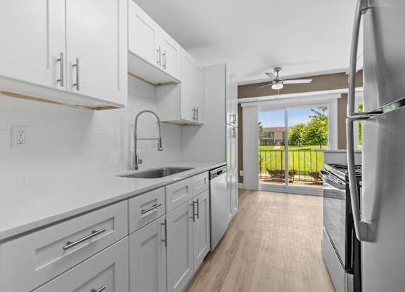 a white kitchen with white cabinets and a sliding glass door at Sunnymede Apartments - Troy, MI, Troy
