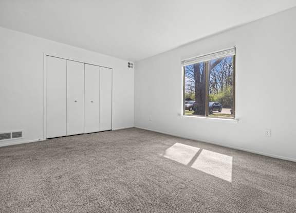 A room with a carpeted floor, a window, and a white door.