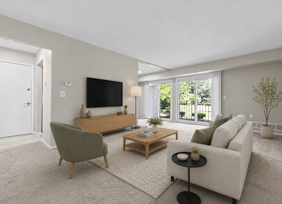 A living room with a grey sofa, a green armchair, a wooden coffee table, and a flat-screen TV mounted on the wall.