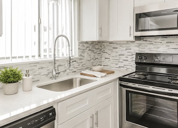 A kitchen with a stove, sink, and cabinets.