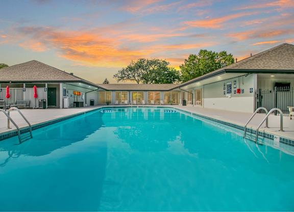 A large swimming pool in front of a building with a sunset in the background at The Waverly on the Lake - Belleville, MI Apartment , Belleville, MI