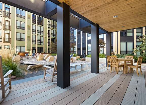 A wooden deck with chairs and a table is surrounded by a modern building.
