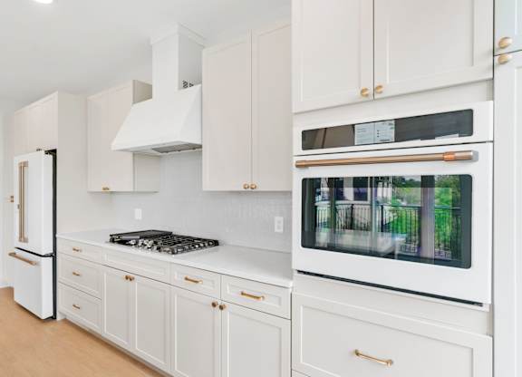 A white kitchen with a black stove top and a white oven with a window.