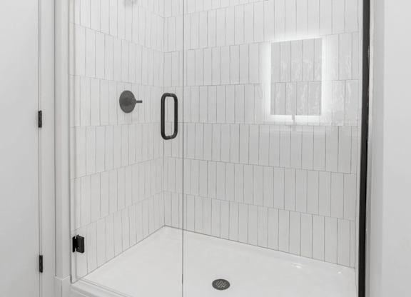 A white tiled shower with a black handle and a black door.