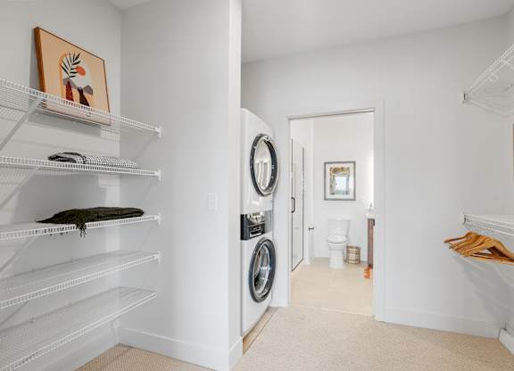 A walk-through closet attached to the bedroom, leading to the bathroom in a one-bedroom, one-bathroom apartment home at Lilia in Lilydale, MN 55118. Features in-unit laundry and storage.