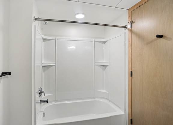 A white bathtub is in a small bathroom.