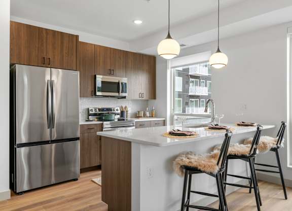 a kitchen with a large island with stools and a stainless steel refrigerator at The Mera, St Louis Park, MN 55426