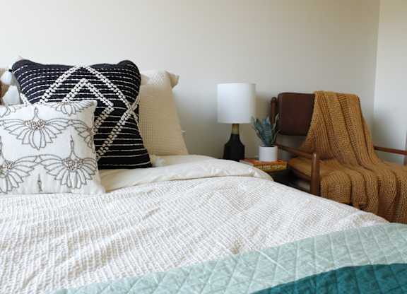 A bed with a white comforter and a blue and green quilt on it.