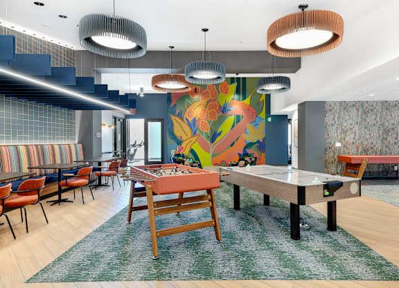 Air hockey and foosball tables under lights near a colorful wall