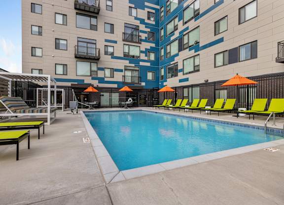 A swimming pool with yellow sun loungers and orange umbrellas in front of a modern building.