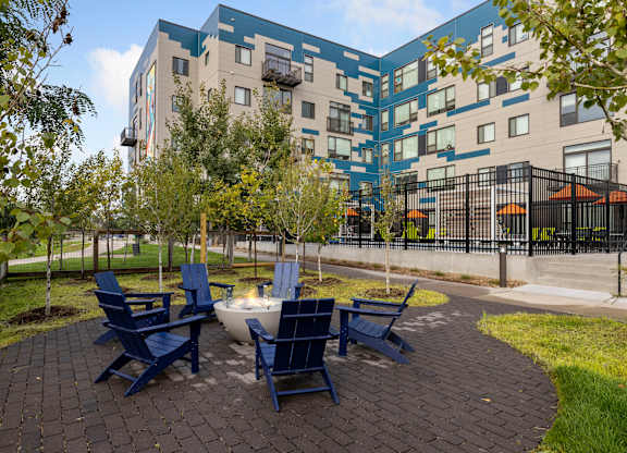 A patio with blue chairs and a table in front of a modern building.