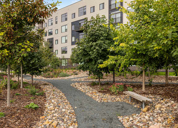 A pathway with a bench and trees in front of a building.