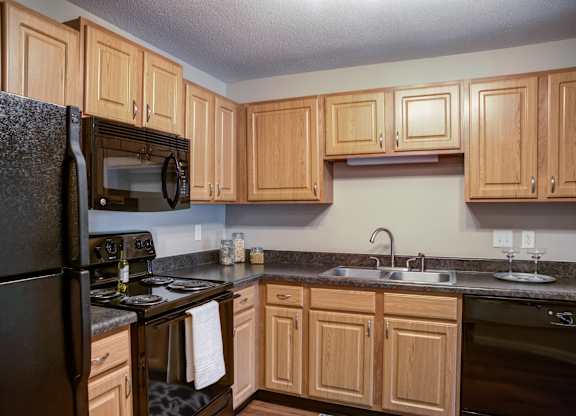 a kitchen with black appliances and wooden cabinets at Cityscape, St Louis Park, 55416