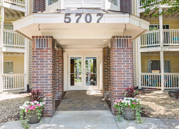 the front entrance of a condo building with flowers on the sidewalk at Cityscape, St Louis Park, MN