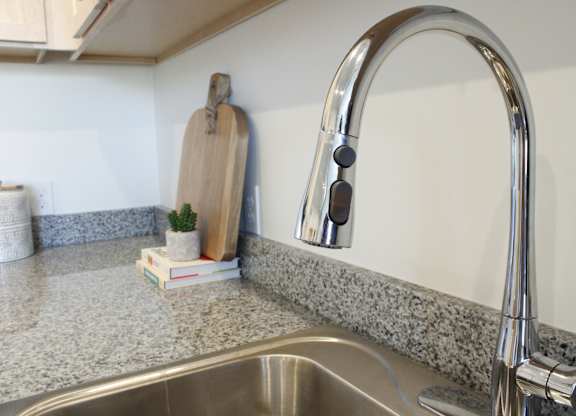 A kitchen sink with a silver faucet and a wooden cutting board on the counter.