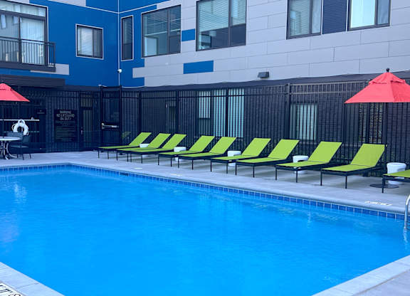 A pool with yellow and green sun loungers and a red umbrella.