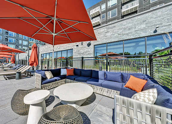 A patio with a blue couch, white table, and red umbrella. at The Mera, St Louis Park, MN, 55426