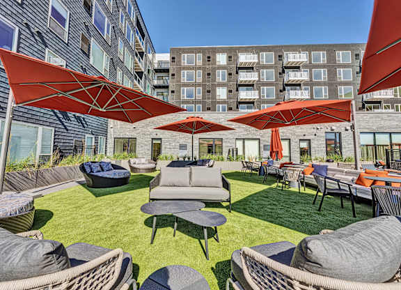 A large outdoor seating area with red umbrellas and grey couches. at The Mera, St Louis Park, MN, 55426