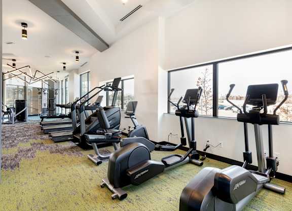 A gym with a row of treadmills and elliptical machines.