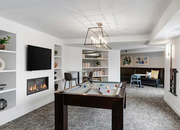 A billiard table is in the middle of a room with a fireplace and a television.