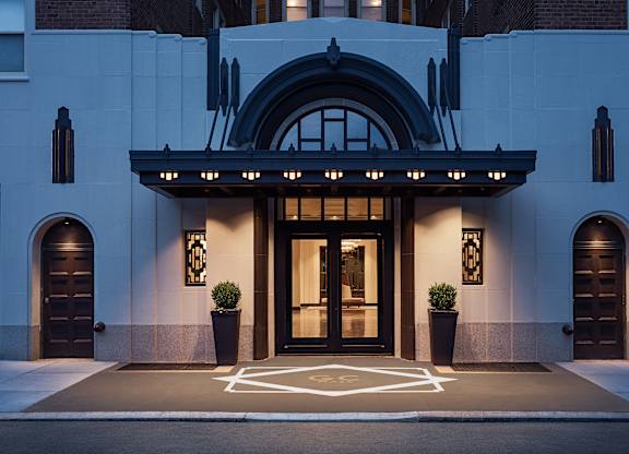 A building entrance with a large arched window and two potted plants on either side.