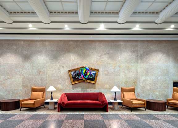 A room with a red couch and chairs with a painting hanging on the wall.