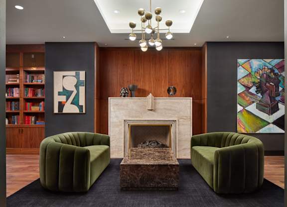 A living room with a fireplace, two green chairs, and a bookshelf.