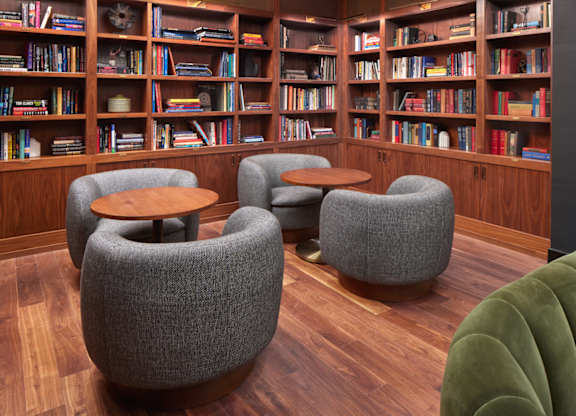 A room with a bookshelf filled with books and a few grey chairs.