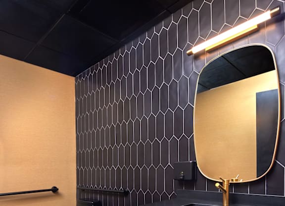 A bathroom with a black toilet and a black and gold mirror.