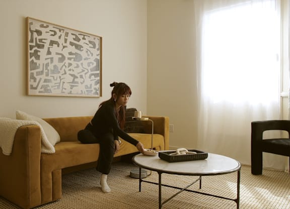 A woman is sitting on a couch in a living room with a painting on the wall behind her.