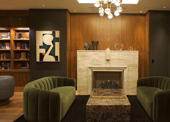 A living room with a fireplace, two green chairs, and a bookshelf.