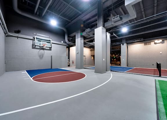 A basketball court is located in a large room with a basketball hoop on the wall.