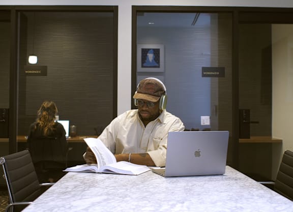 A man in a white shirt is sitting at a table with a laptop and a book.