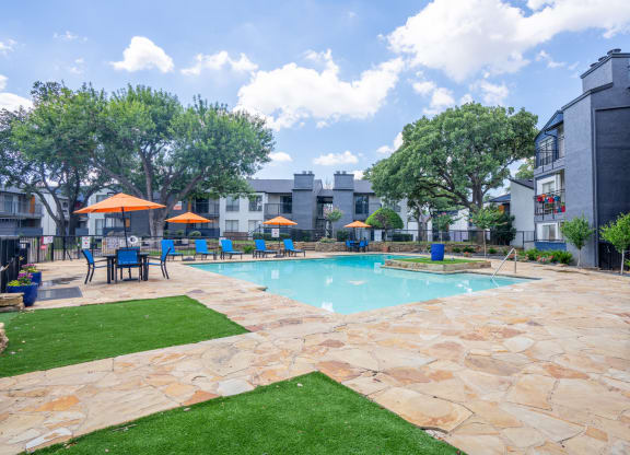 a swimming pool with tables and umbrellas in front of a building at District 2308, Arlington Texas?