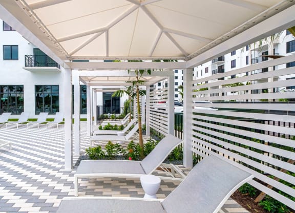 a patio with two lounge chairs and a white building at Altis Grand Kendall, Florida, 33186