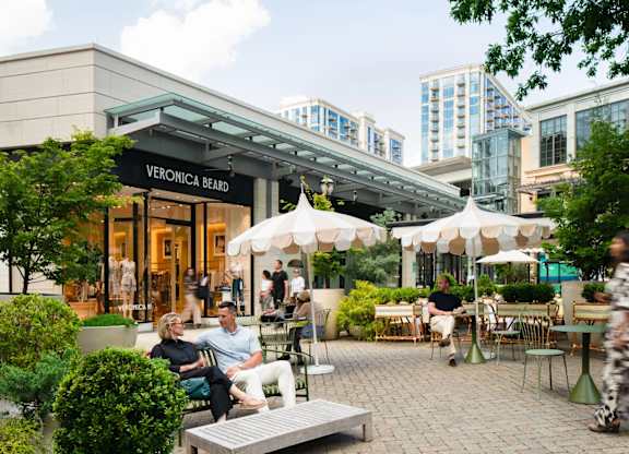 A woman is sitting on a bench outside of a Veronica Beard store.